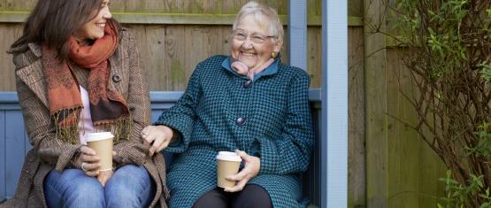 Two women drinking tea on a bench